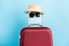 太阳镜、医用面罩和蓝色红色行李的草帽