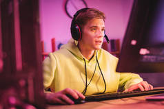 使用计算机键盘和鼠标在模糊的前景上集中在耳机中的游戏玩家