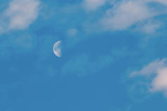 日落时分,月亮在蓝天上升起,乌云密布.半月相，白天有云。天空中月亮的低角度视图.