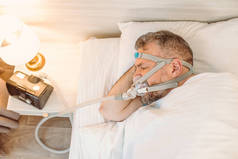 有慢性呼吸问题的睡眠男子考虑在床上使用CPAP机。保健、阻塞性睡眠呼吸暂停疗法、 CPAP 、打鼾概念