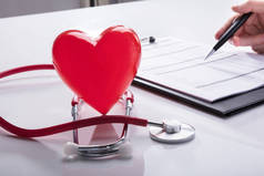 听诊器和红心心脏接近医生的手分析剪贴板上的报告