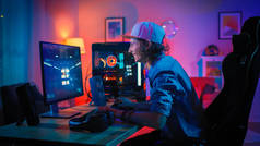 专业玩家玩第一人称射击在线视频游戏在他的强大的个人计算机与五颜六色的霓虹灯。年轻人戴着帽子。客厅点亮着温暖的红灯。晚上.
