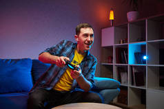 游戏迷坐在沙发上，手里拿着控制台游戏垫，在室内游戏平台上玩电子游戏。在家休息，度过一个愉快的周末.