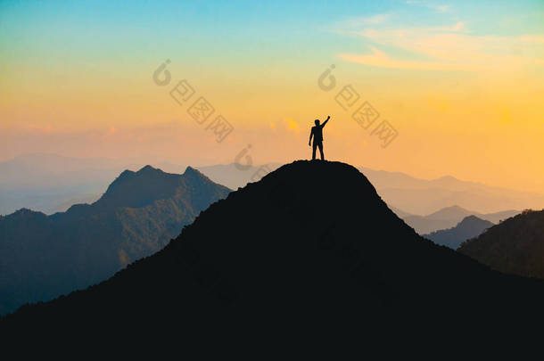 在日落时分，一个手拿着愉快的<strong>高举</strong>在山顶上的人的轮廓：努力与成功的概念