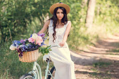 有吸引力的女孩在草帽坐在自行车与花在柳条篮子在公园