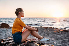 夕阳下美丽的海滨, 坐在格子上的漂亮的年轻女子的侧面视图