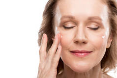 成熟妇女应用化妆品霜在脸上孤立在白色