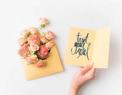 手拿着纸与信任你的灵魂标志旁边的粉红色的花朵在信封上孤立的白色