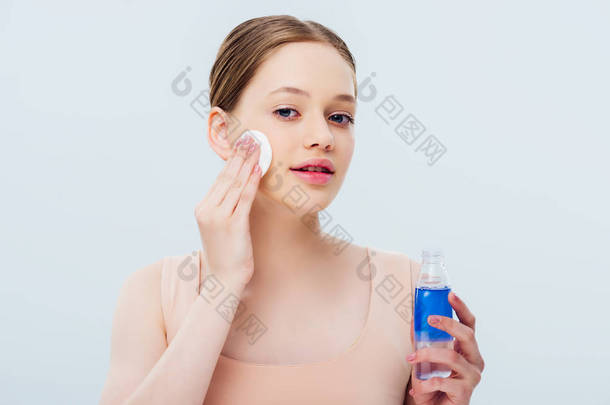 漂亮的少女应用<strong>化妆水</strong>脸上与棉垫隔离在灰色