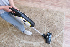 无绳真空吸尘器用来清洁房间里的地毯。带着新手提式吸尘器的家务活。家庭清洁、护理和技术概念.
