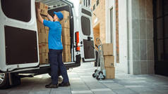 送货人使用满载纸板箱和包装箱的手推车，装载包裹进入货车货车。专业快递员协助您快捷快捷快捷地移动、运送所购货品