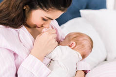 年轻母亲母乳喂养小婴儿的肖像在床上在家里