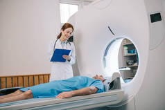 美丽的放射科医生拿着剪贴板，同时准备病人断层扫描
