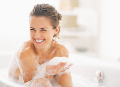 快乐的年轻女子在浴缸里玩泡沫的画像