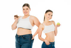 快乐苗条和超重的女孩摆姿势与甜甜圈和青苹果隔离在白色