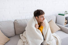 穿着毛毯的年轻人坐在沙发上，在客厅里取暖