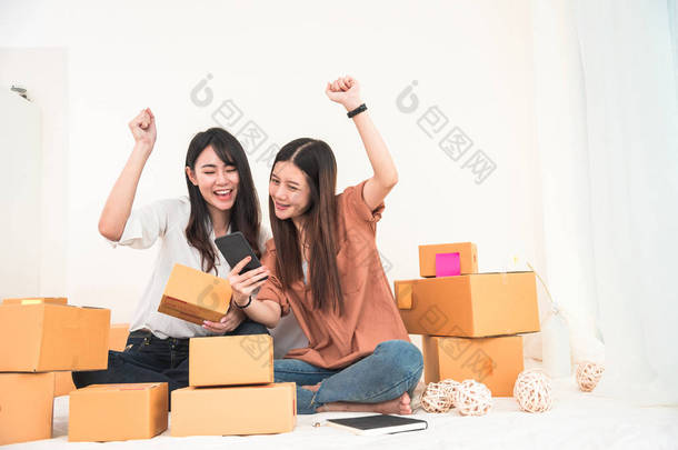 两名年轻的亚裔女子创办小企业企业家中小企业<strong>分销</strong>仓库与包裹信箱。所有者家庭办公室。在线营销和产品包装及送货服务。快乐的手势