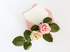 粉色信封与白卡和玫瑰。平躺.