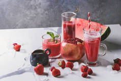三种不同的红果浆果西瓜, 草莓, 覆盆子, 石榴鸡尾酒或冰杯中的冰, 新鲜薄荷和配料在白色大理石桌上.