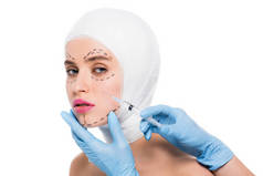 穿着蓝色乳胶手套的整形外科医生的裁剪视图, 她拿着注射器, 脸上有被查出的痕迹在白色