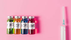 顶端的注射器和瓶子的爱, 希望, 喜悦和和平疫苗标志在排在粉红色桌面上