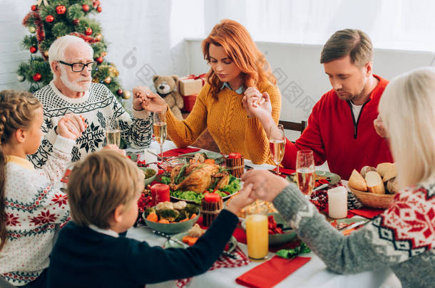 一家人手牵着手，坐在节日餐桌前吃感恩节大餐