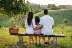 全家人坐在长椅上的背景图，靠近前面的柳条篮，风景秀丽