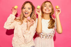 两个年轻迷人的漂亮女孩穿着时髦的夏日服装。妇女用五颜六色的杏仁饼, 抱着马卡龙近脸。摆在粉红色背景