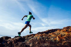 女赛跑选手在日出海滨跑到岩石山顶