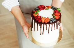 年轻的黑发女厨师，手持自制的蛋糕，上面装饰着巧克力和新鲜的浆果.