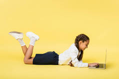 躺在黄色背景下的儿童使用笔记本电脑的侧视图