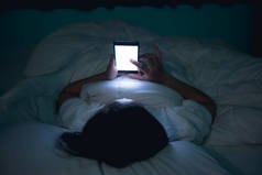 亚洲女人晚上在床上用智能手机玩游戏