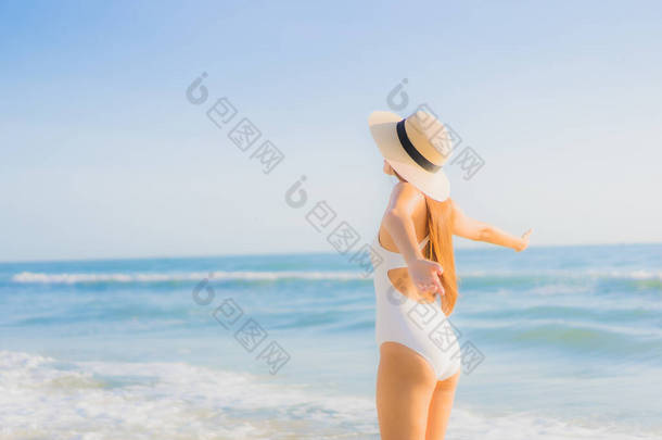 美丽动人的年轻亚洲女人快乐的笑着环抱着海滩和蓝天，享受休闲旅游之旅