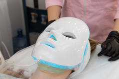 女人躺在床上，带着光疗面罩和放松。面部皮肤治疗用带光罩,会期美容术.