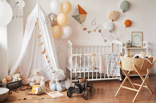 斯堪的纳维亚风格的白色室内儿童房，卧室，托儿所。有天篷的婴儿床。木制货架和玩具天篷帐篷、纺织品风筝和气球.