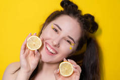 年轻的女人，有柠檬片，黑发女孩，裸露的肩膀，持有柠檬接近脸的黄色背景。柑橘类水果，健康食品。美味的多汁水果.