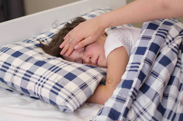 有爱心的母亲把头靠在生病的儿子额头上。<strong>儿童保健</strong>概念。可怜的小男孩躺在床上.