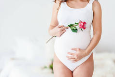 一个穿着白衣的孕妇手持美丽的花朵。可爱的概念健康怀孕，母亲节，母亲节的概念。带有复制空间的横幅.