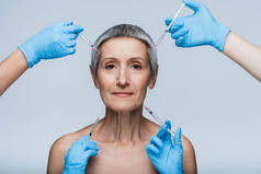戴蓝色乳胶手套的美容师拿着注射器，近中年患者注射美容品，分离于灰色区域