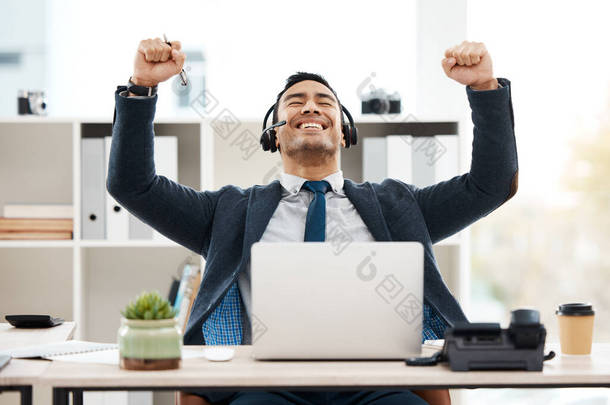 a young male call center agent cheering while using a laptop in an office at work.