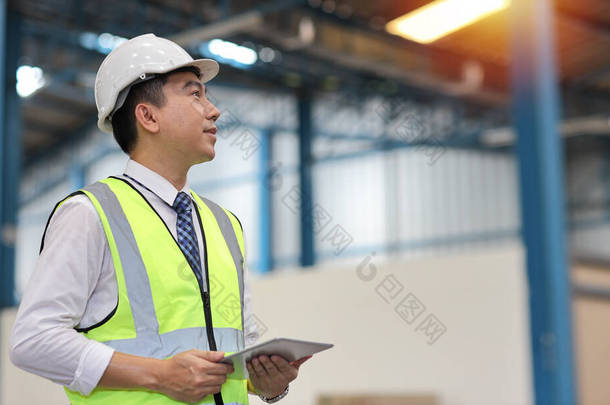 建筑师或工程师和工人站在那里用平板电脑检查大型仓库。亚洲商业经理展望未来与仓库建设的背景.