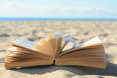 Open book on sandy beach near sea