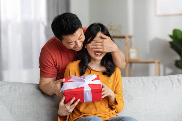 爱亚洲男人盖住女人的眼睛，送给他年轻漂亮的妻子礼品盒，为情人节或生日、家庭内部、自由自在的空间带来惊喜。周年庆祝活动
