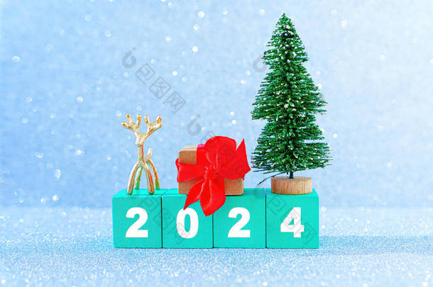 2024年新年背景是由绿色的木制字母块、玩具圣诞树、小鹿雕像和装饰的礼品盒做成的，背景上闪烁着模仿雪花的光芒.