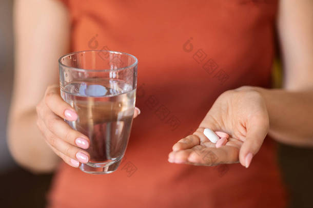 无法辨认的女人手里拿着一杯水和一堆堆药丸，被女人用维生素补充剂擦伤美体和免疫力，或接受治疗，被剪裁的形象