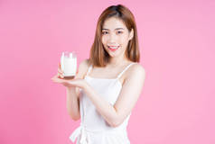 在粉红背景下喝牛奶的年轻亚洲妇女形象