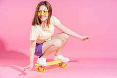照片上的亚洲少女带着粉色背景的滑板