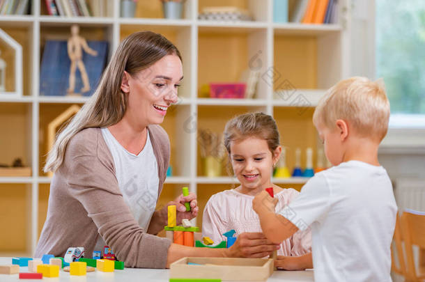 幼儿园老师和孩子们一起在五彩缤纷的幼儿园教室里玩耍.母亲和孩子们玩耍.