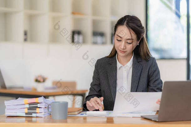 在明亮的现代化办公室里，微笑着在平板电脑上工作的亚洲女商人用图表文件计算财务报告支出
