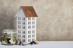 房子模型,货币箱与美元钞票,钥匙和银币在灰色背景的白色桌子上,房地产概念